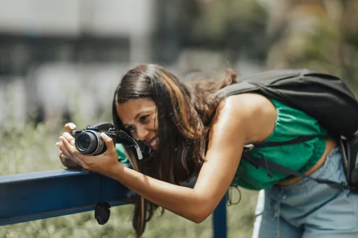 Young woman photographing cityscape with DSLR, leaning over a blue railing outdoors.